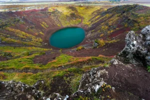 Kerið volcanic crater in early autumn with green moss, red volcanic slopes, and a vivid turquoise lake.