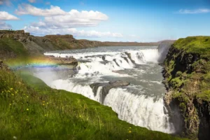 Gullfoss waterfall in summer with a bright rainbow arching over the lower cascade on Iceland’s Golden Circle.