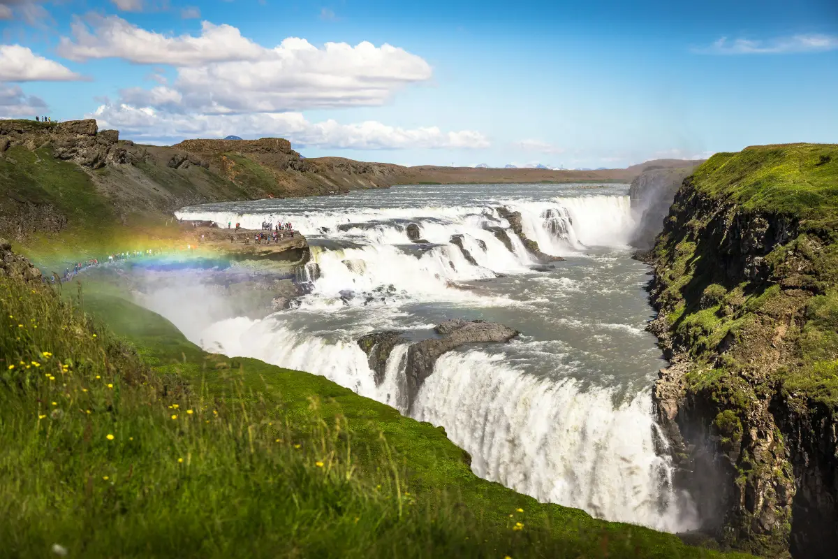 Gullfoss waterfall in summer with a bright rainbow arching over the lower cascade on Iceland’s Golden Circle.