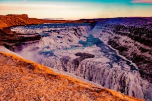 Gullfoss waterfall in winter at sunset with icy edges and warm golden light over the canyon.