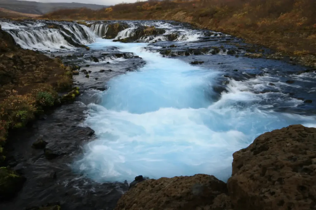 Brúarfoss waterfall with bright blue glacial water flowing through black lava rocks