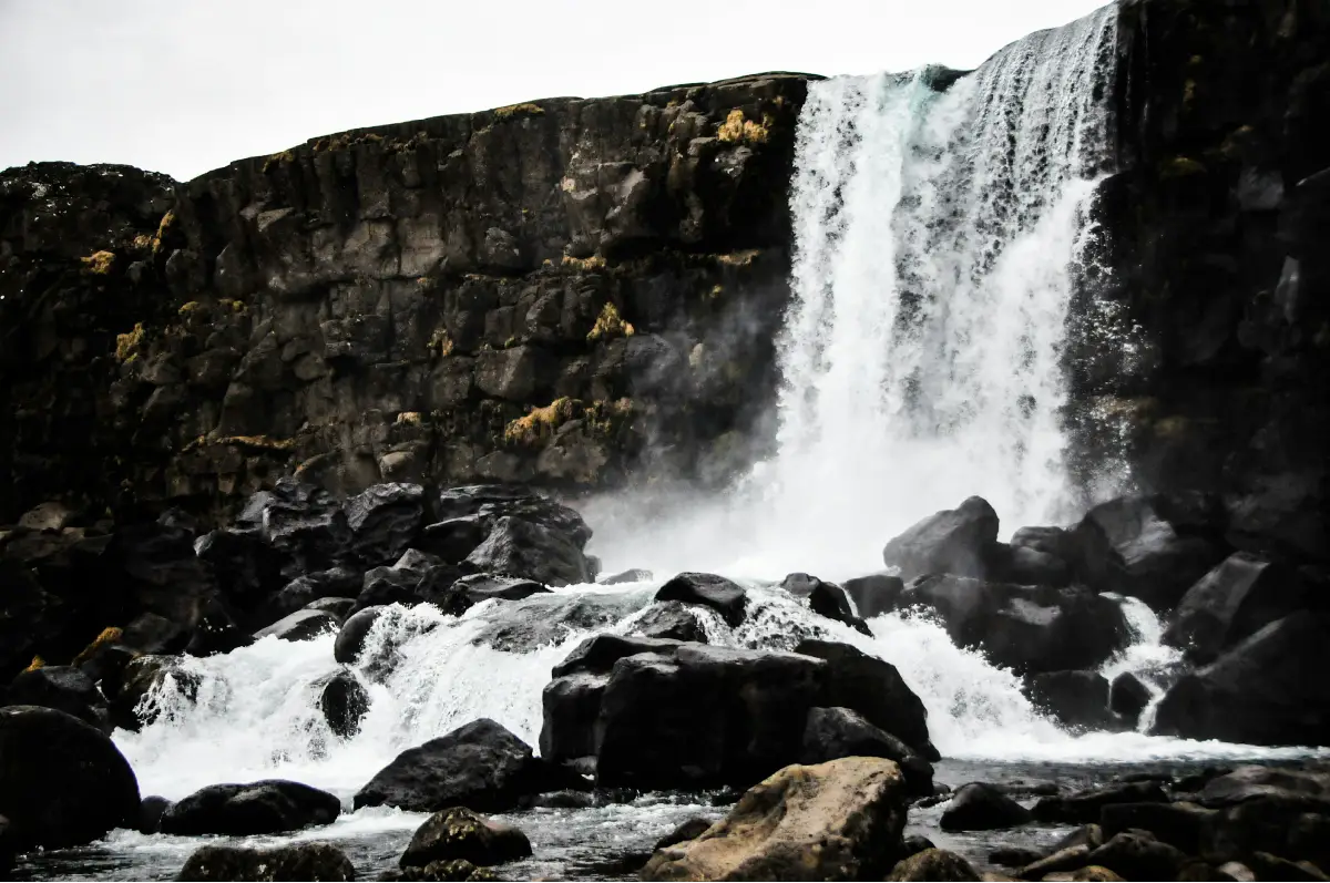 Powerful Öxarárfoss waterfall cascading over dark basalt cliffs in Þingvellir National Park, Iceland.