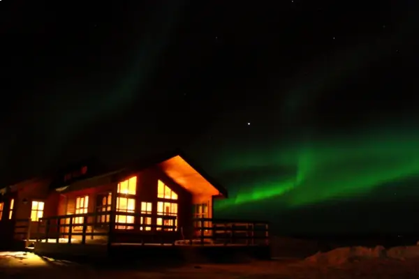 The wooden cabin at Vorsabær 2 is illuminated by northern lights near the Golden Circle.