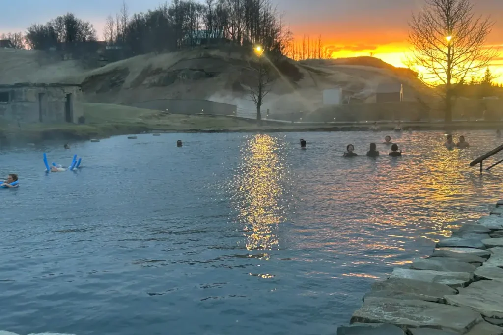 People bathing in the Secret Lagoon geothermal pool with sunset reflecting on the water in Iceland