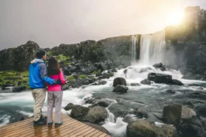 Couple standing on a wooden platform overlooking Öxarárfoss waterfall in Þingvellir National Park Title