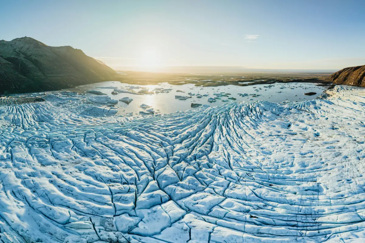 Panoramic view of a glacier with ridged ice patterns and a lagoon in the distance at Vatnajökull