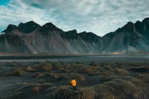 A traveler standing on black sand dunes beneath the dramatic peaks of Vestrahorn in southeast Iceland