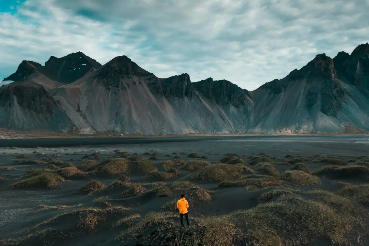 A traveler standing on black sand dunes beneath the dramatic peaks of Vestrahorn in southeast Iceland