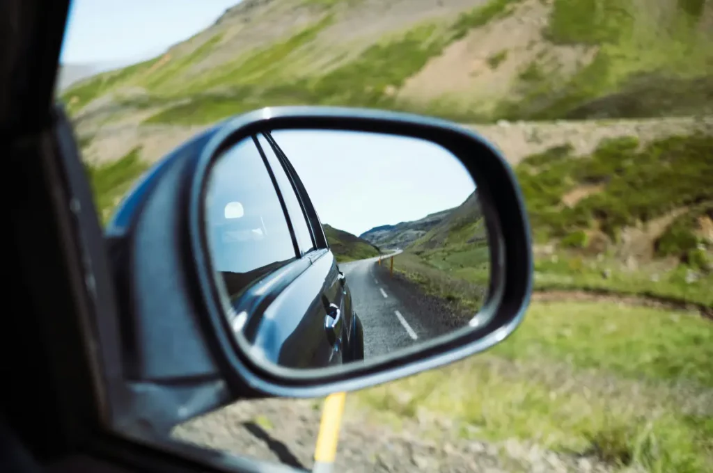 View of a winding Iceland road through a car side mirror, showing a scenic countryside drive