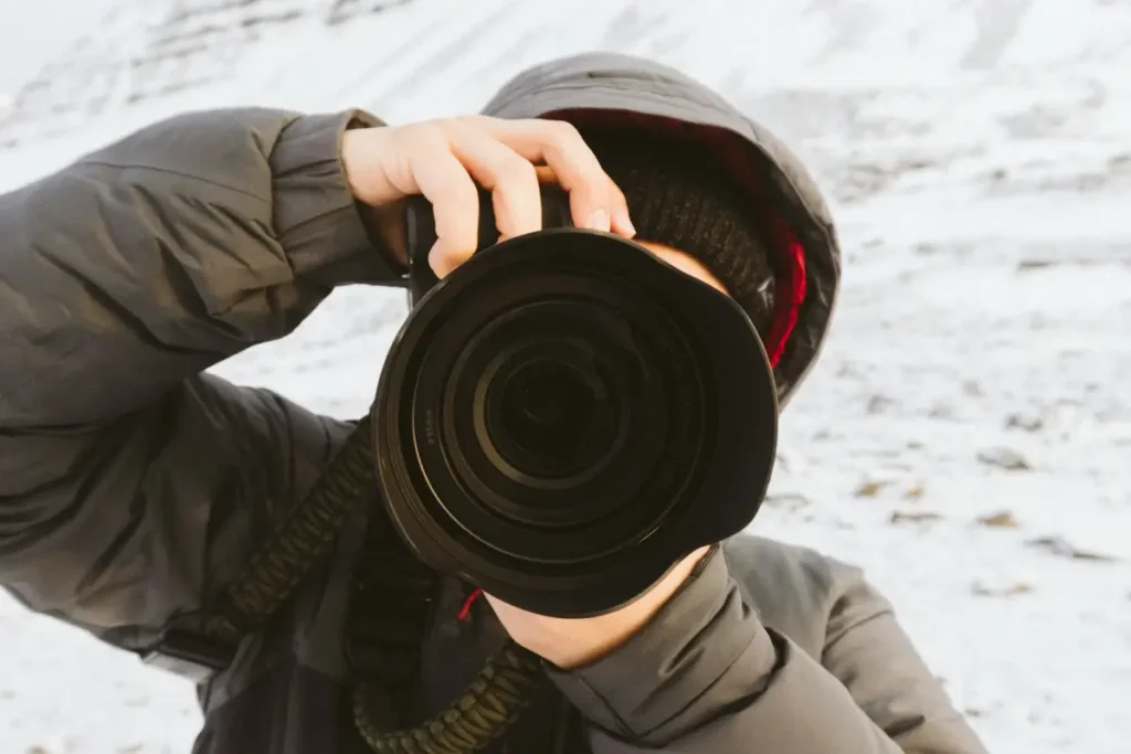 A photographer holding a camera in snowy Iceland landscape, capturing winter scenes near the Golden Circle