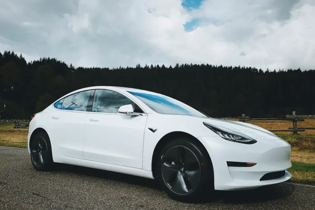 A white Tesla car driving on a scenic road in the Icelandic countryside is ideal for Golden Circle road trips