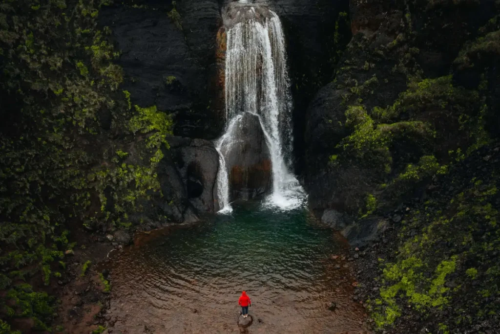 Helgufoss waterfall near Mosfellsdalur with hiker standing by on a stone below