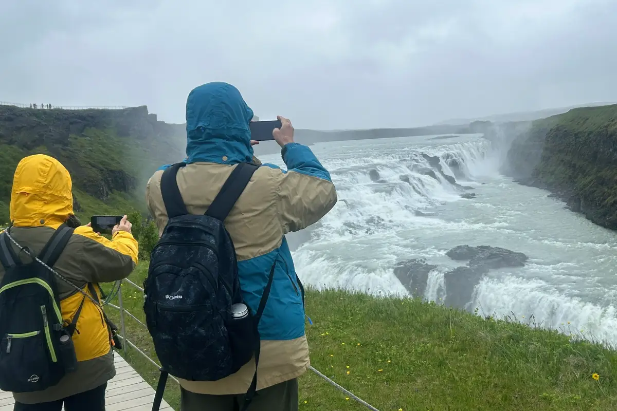 Travelers with backpacks photographing the wide view of Gullfoss waterfall