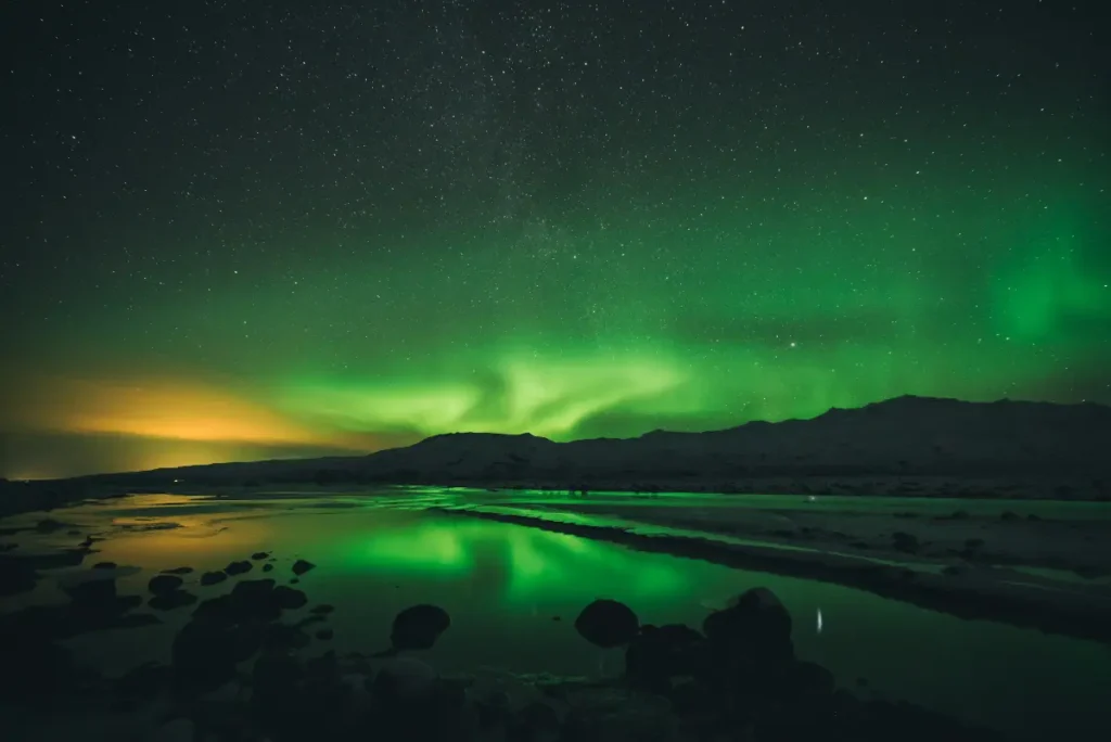Green Aurora Borealis reflected in water beneath a starry sky in Iceland