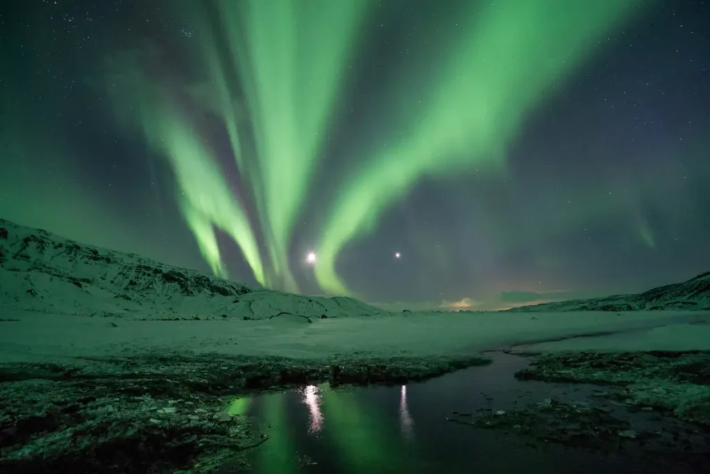Bright green Aurora Borealis above a snow-covered valley in Iceland