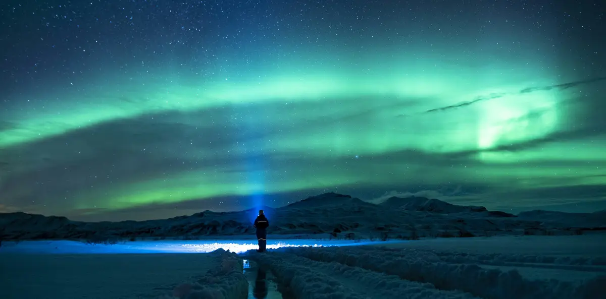 Green Northern Lights above a person standing in a snow-covered landscape in Iceland