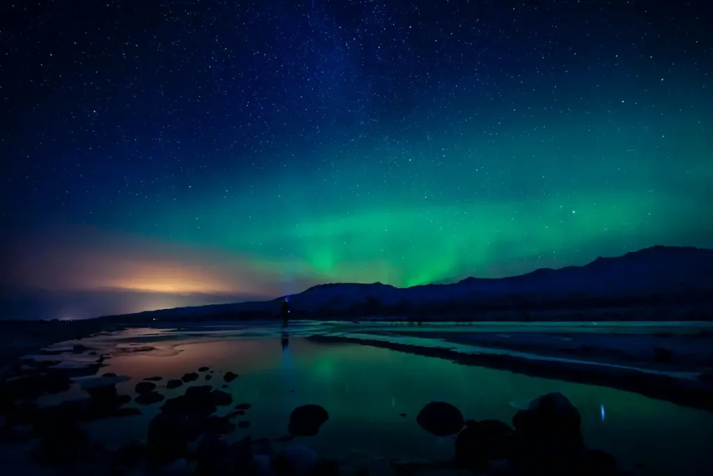 Northern Lights stretching across a star-filled sky above a winter road in Iceland