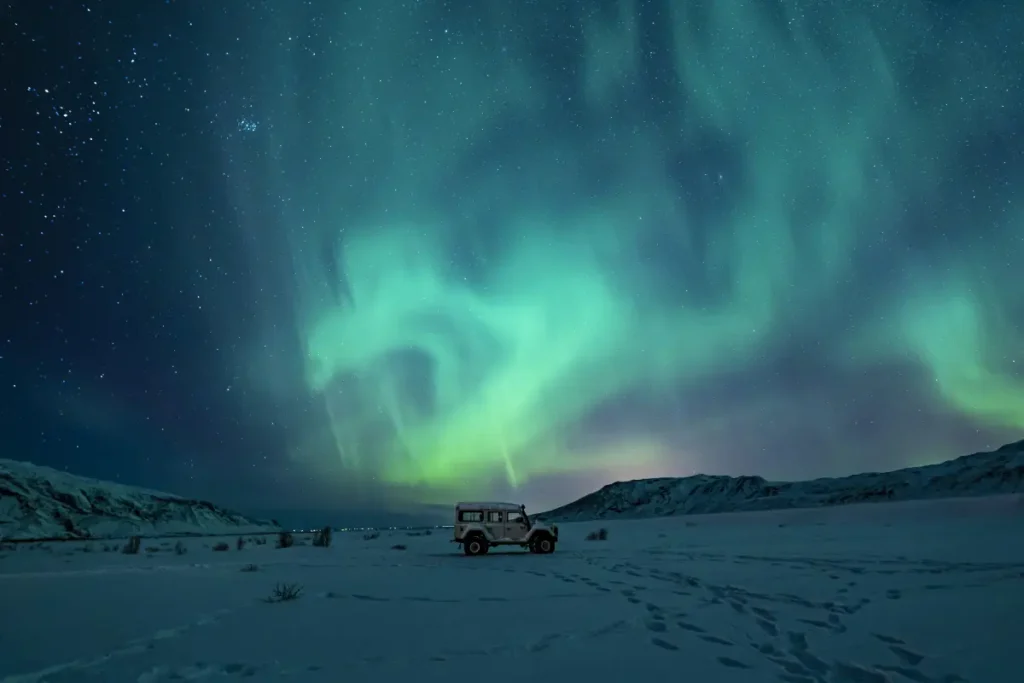 Northern Lights above a 4x4 vehicle in a snow-covered Icelandic landscape
