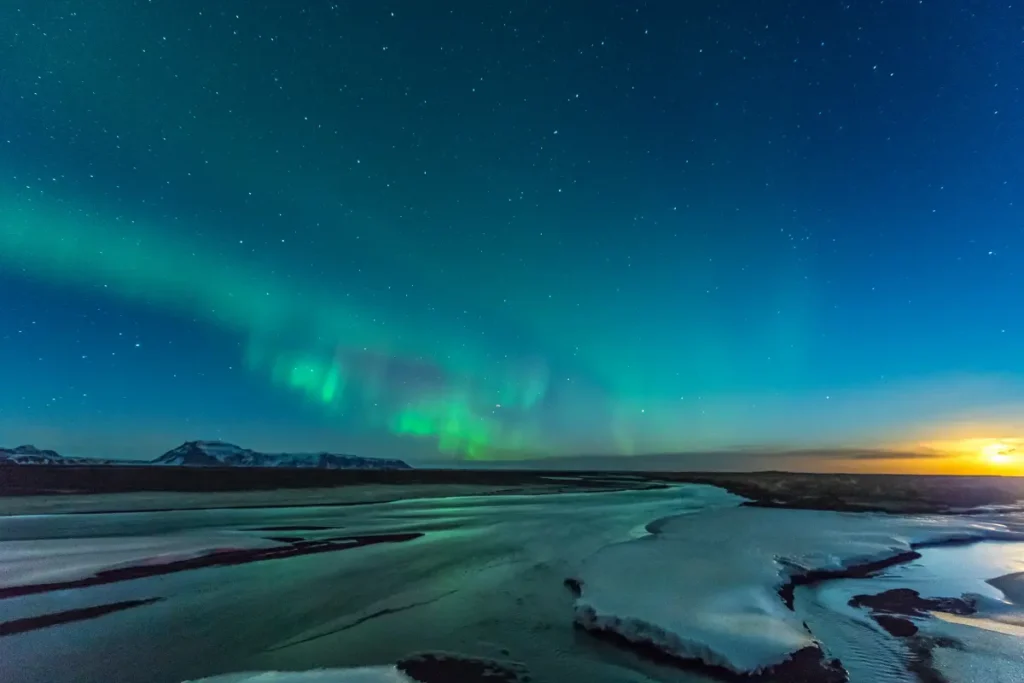 Northern Lights glowing above a frozen river and winter landscape in Iceland